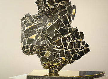 L'opera realizzata dallo scultore Giuseppe D'Angelo coesioni rappresenta un volto frammentato in marmo nero e ottone